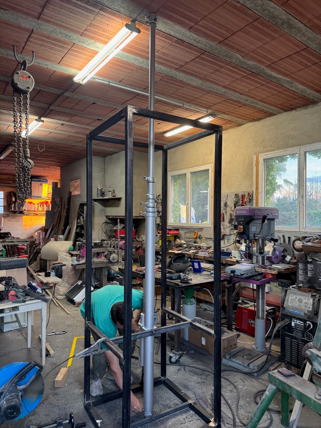Vue de l'atelier : châssis en cours d'assemblage, perceuse à colonne, postes de soudure.